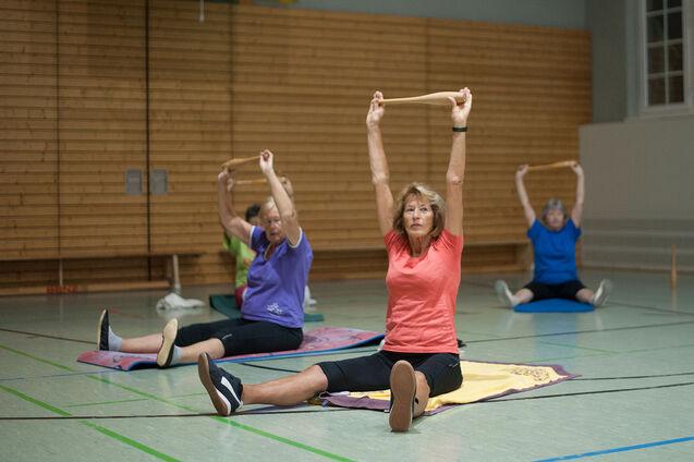 Gruppe von Frauen beim Fitnesstraining mit Widerstandsb&auml;ndern in einer Sporthalle, einige sitzen auf Matten.