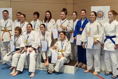 Gruppe von 14 Judoka in kimonos mit Medaillen und Urkunden auf einem Podest bei einer Preisverleihung.