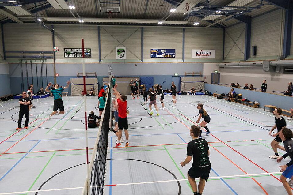 Zwei Teams spielen Volleyball in einer Sporthalle mit mehreren Spielern und einem Netz in der Mitte.