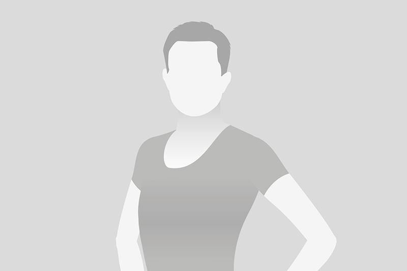 Porträt einer Person mit kurzem Haar, in schwarzem Shirt, auf grauem Hintergrund, Gesicht nicht sichtbar.