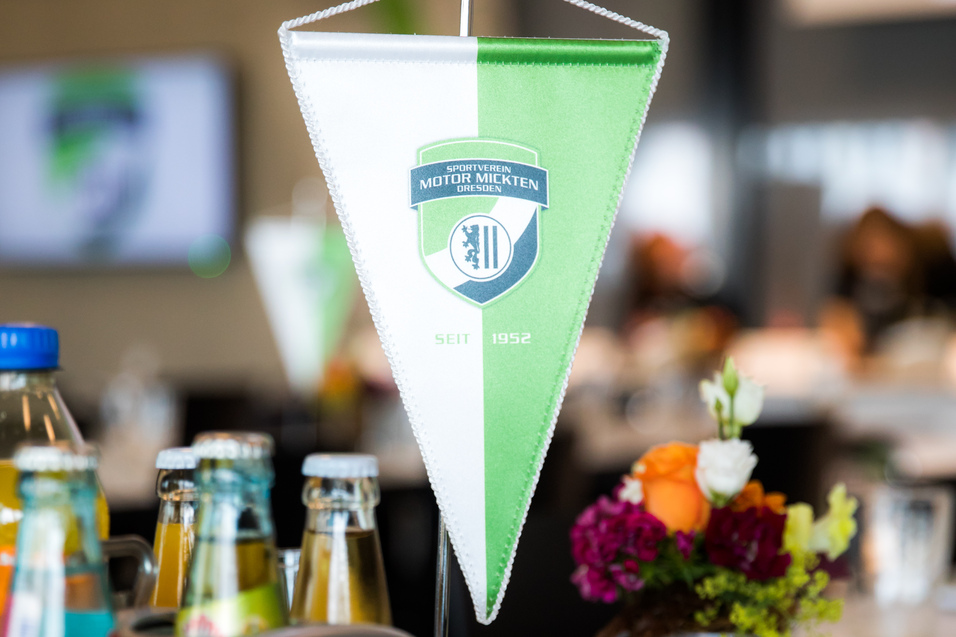Tisch mit einem Wimpel des Sportvereins Motor Mickten, Getr&auml;nken und einer Blumenvasen im Hintergrund.