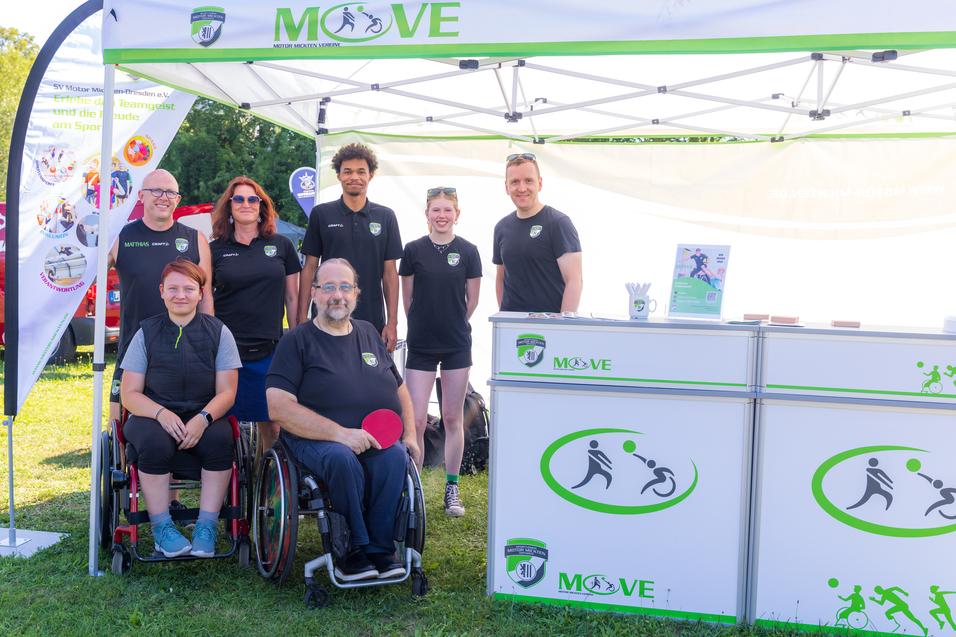 Gruppe von sechs Personen, darunter ein Mann im Rollstuhl, vor einem Veranstaltungsstand mit dem Logo &bdquo;MOVE&ldquo;.