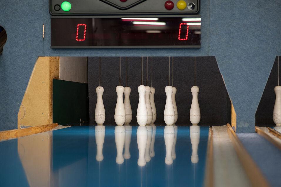 Nahaufnahme einer Kegelbahn mit sieben Kegeln und einer digitalen Anzeigetafel im Hintergrund.