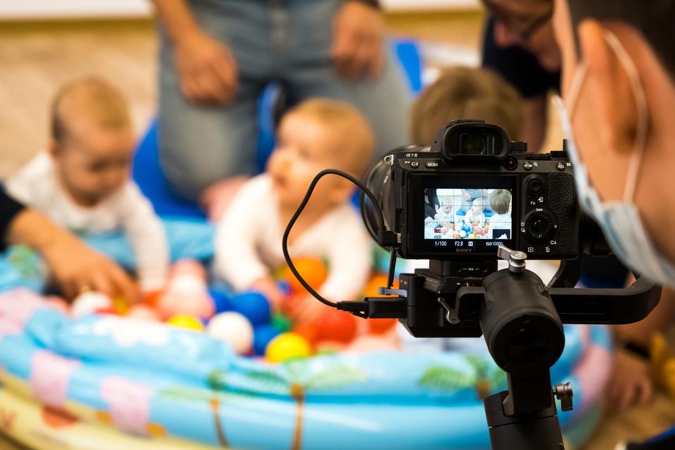 Ein Kind spielt mit bunten Bällen in einem aufblasbaren Planschbecken, während ein Fotograf das Geschehen aufnimmt.
