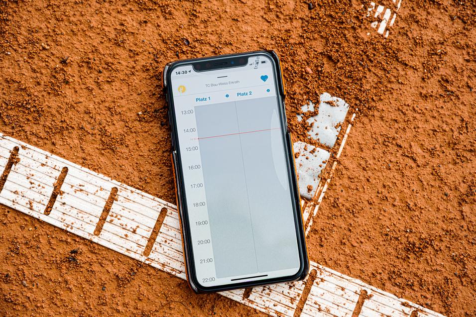Smartphone auf rotem Tennisplatz, zeigt den Wochenplan mit Zeiten für zwei Plätze.